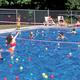 Clear photo of the main swimming pool with fenced perimeter and campers using the facility — matches the homepage/gallery image and facilities page context showing the campground pool.