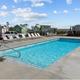 Outdoor rectangular swimming pool with handrails and lounge chairs on concrete deck, backed by colorful cabins and
