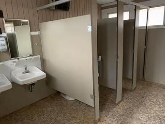 Partial interior view of comfort station.  2 small bathroom stalls, 2 windows, 2 porcelain sinks with mirrors.  Flooring is tile,