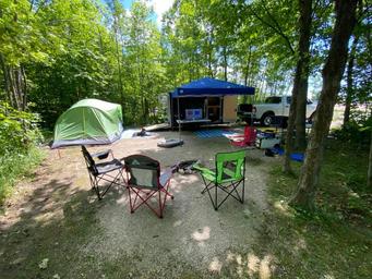 Tent campsite with chairs and vehicle visible in a wooded site — good example of a tent/campsite offering from the property photo gallery.
