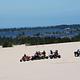 Off road vehicles on flat expanse of sand in front of blue lake ringed by conifer trees.