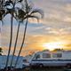 A rv is parked next to palm trees at sunset.