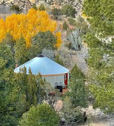 Elevated/landscape view showing a yurt nestled among trees with fall color — useful aerial/setting photo demonstrating the property’s natural surroundings; sourced from the site’s yurt/gallery content.
