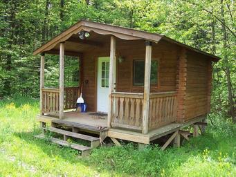 Front view of a rustic cabin on grass with porch — good representation of overnight cabin lodging on the property (site gallery context).