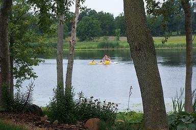 Lakeside shot showing people paddling on Snow Lake framed by shoreline trees — good scenic view of on-site water recreation; image appears on the 'Our Campground' page.