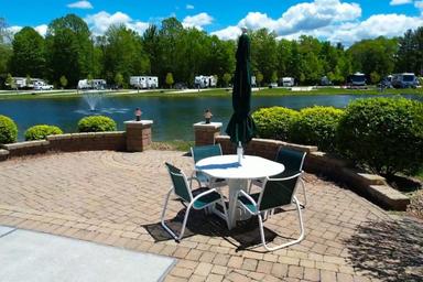 Patio with table and umbrella overlooking a pond with RV sites across the water — illustrates a premium lakeside site and patio area promoted on the rentals page.
