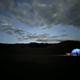 Nighttime. Glowing tent on dark sand dunes. A few stars and clouds in the sky.