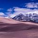 Rolling sand dunes with snowy mountains in the background.