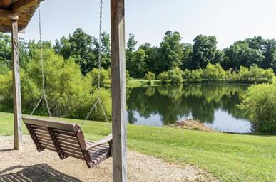 Covered swing overlooking a pond/reflective lake with tree-lined shore — good scenic shot of the campground’s lake and relaxation area (homepage gallery background).