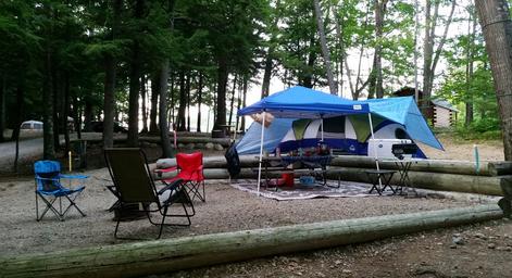 Tent campsite in a wooded area with defined log-bordered pad, chairs and canopy — shows tent camping setup and wooded campsite character on the grounds.