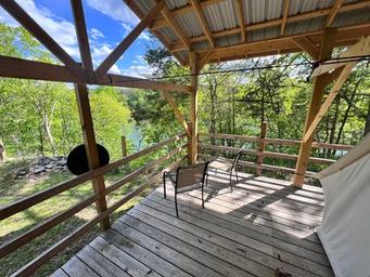 Deck of a glamping cabin/tent with chairs and railing overlooking treed shoreline — clear on-site accommodation photo suitable for property gallery. Source: contact page (lakecumberlandglamping.com/contact).