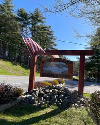 Entrance sign reading ‘King Phillip Campground’ at roadside with American flag — identifies the property and provides a clear branded exterior landmark.