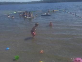 Shallow swimming area with people and safety float lines in the lake — illustrates the park’s beach/swim amenities (visible on-site activity).