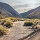 Gravel dirt road with parallel roadside campsite surrounded by mountains.