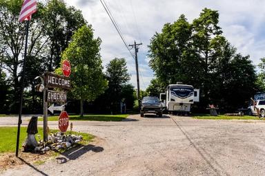 Entrance/drive area with RVs and a welcome/check-in sign — clear depiction of the RV sites, arrival area and campground access (contact/visit page background).
