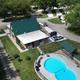 Aerial/drone hero shot showing campground clubhouse, distinctive kidney-shaped pool, paved roads, RV sites and activity lawn — on the campground’s main page (hero image) supporting this is the property grounds.