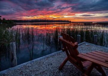 Sunset lakeside view with Adirondack chair on a small shore area — highlights waterfront guest seating and scenic views from the property (homepage gallery image).