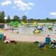 Beach-area wide shot showing sandy shore, grassy seating and inflatable aqua-park on the water — useful close-in view of the resort’s waterfront amenities (beach-area.jpg).