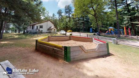 Play area/sandbox and nearby buildings with campground watermark — depicts family recreation area and facilities on the grounds.