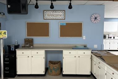 Organized classroom corner with white cabinets, bulletin boards, and a welcome sign.