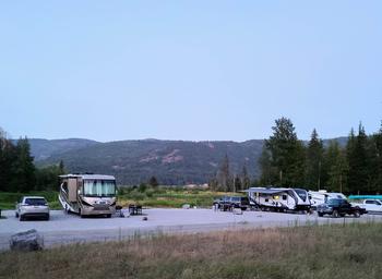 Wide-angle dusk shot showing a row of RVs and cars on the campground pads with surrounding mountains — good overall view of site layout and setting from the property's gallery page.