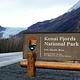 Kenai Fjords entrance sign on the road with Exit Glacier in the background.