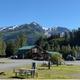 Ground-level wide shot showing the main lodge/cabin, picnic tables, RV spaces and dramatic mountain backdrop — useful to show facilities and setting (page context: site homepage).