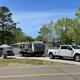 Clear daytime photo of an RV pitch with truck, awning and picnic setup — shows typical RV site layout and road access on the property (from the site gallery).