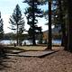 Sunlit tent pad in front of conifers in silhouette with lake and hill in background.