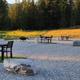 Gravel campsite area with multiple fire pits, picnic tables, and hoses visible — useful closeup of campsite amenities and surface treatment on the property.