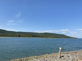 A rocky beach and a wide blue lake between low green hills