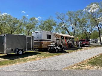 Large RV parked on a gravel/driveway site among trees with hookups and golf cart — illustrates full-hookup RV accommodations and wooded campsites. (gallery images on the site).
