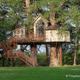 Exterior view of the Chapelle treehouse elevated on large trunks with deck and stairs, set in grassy grounds — good overall portrait of accommodation and landscape (homepage/treehouses imagery).