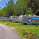 Side-angle ground-level view showing a line of trailers and grassy lots with trees — shows campsite spacing and vegetation on the grounds (from the park website).