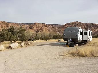 Campsite with trailer parking in parking area. Red rock cliffs line the horizon in the background.
