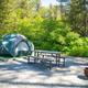 Tent on a raised pad with picnic table and fire ring in a wooded campsite — good depiction of tent camping sites at the property. Image is from the Seward 'waystostayphotos' set.