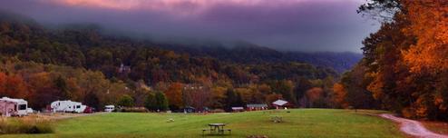 Panoramic meadow with RVs, picnic table and campground buildings with forested hills beyond — another clear overall property view (used on the site's homepage imagery).