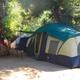 Tent camping site image showing a multi-room tent beneath trees and campground surroundings — useful to show non-RV camping options.
