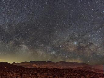 Mountains in foreground, clear night sky filled with stars in background.
