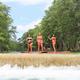Three women in swimsuits standing on paddleboards in a river with green trees on both sides.