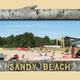 Framed photo labeled 'SANDY BEACH' showing a beach area with people, lounge chairs and RVs in the background — depicts the campground's beach amenity referenced on the site.