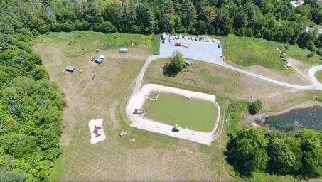 Top-down drone image focused on the play/pond and adjacent grounds with walking areas and playground visible — helpful for showing the central recreational feature.