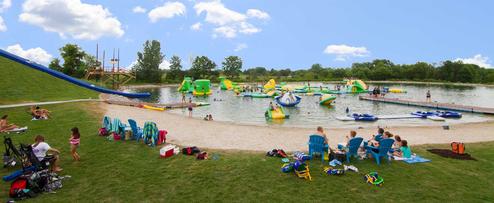 Beach-area wide shot showing sandy shore, grassy seating and inflatable aqua-park on the water — useful close-in view of the resort’s waterfront amenities (beach-area.jpg).