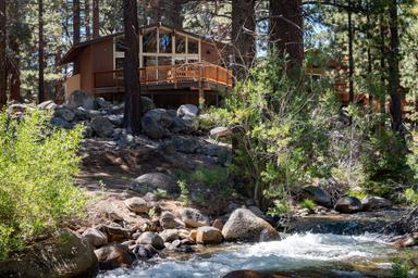 Another riverside/lodge view: close-angle of a cabin and deck above the creek with boulders and trees (from site’s 'General 2' gallery) — useful for highlighting creekfront lodging.