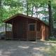 Exterior view of a wooded cabin with small porch and surrounding trees — additional cabin style photo from the property’s accommodation images, good for variety.