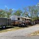 Large RV parked on a gravel/driveway site among trees with hookups and golf cart — illustrates full-hookup RV accommodations and wooded campsites. (gallery images on the site).