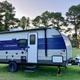 Exterior photo of an RV/trailer on a grassy campsite with trees and a playground visible — shows the park’s RV/site character (from the site homepage).