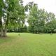 A green lawn with trees scattered throughout. In the distance a picnic table can be seen denoting a campsite.
