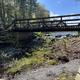 Scenic on-site footbridge over a stream/river with surrounding trees—good overview of natural water feature and grounds (appears on homepage/gallery).