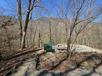 A green food storage locker sits near a picnic table on a campsite overlooking the river.
